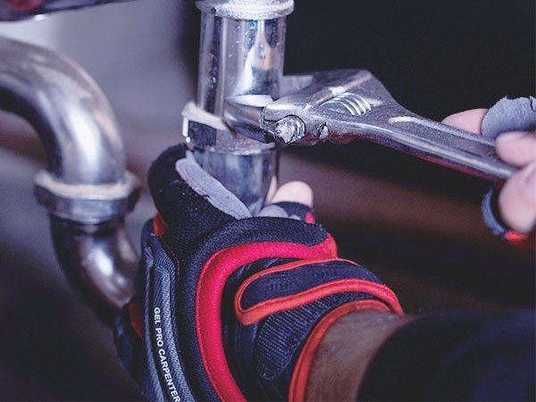 Plumber's hands tightening a pipe fitting with a wrench, from the B. Spontak website