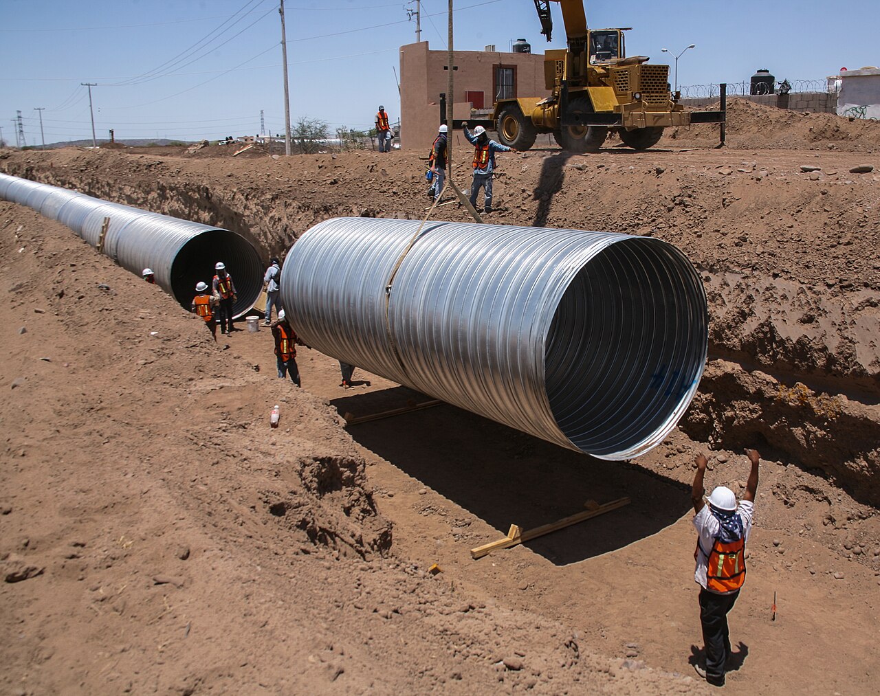 Large metal pipe being positioned in a trench by a crew